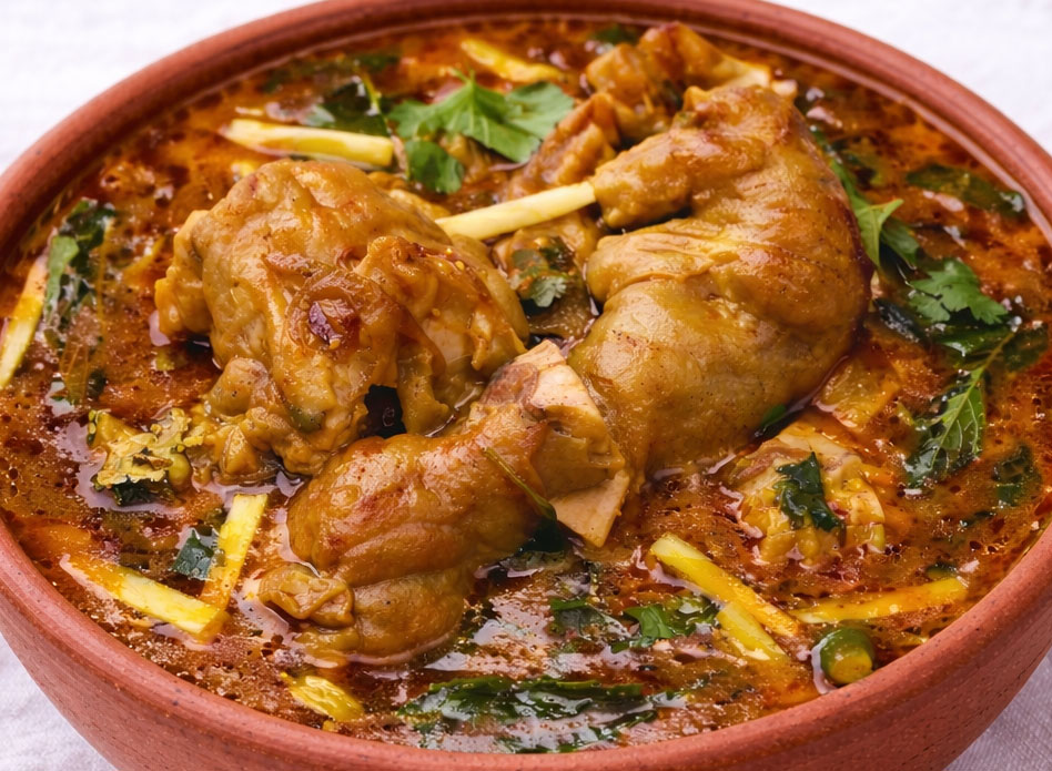 Lahori paya beef trotters curry in terracotta bowl served with naan, salad, green tea, and lemon on white background