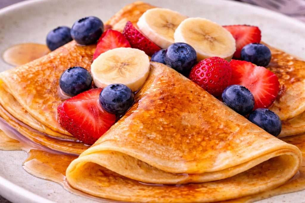 Fluffy pancakes with maple syrup, strawberries, blueberries and banana slices close up