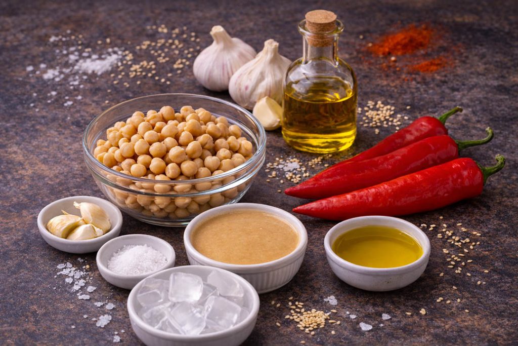 Ingredients for roasted red pepper hummus including chickpeas, tahini, garlic, olive oil and red peppers