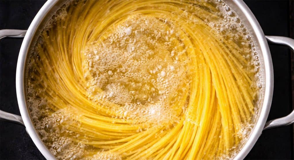 Top view of spaghetti boiling in a stainless steel pot on a black hob with bubbling water.